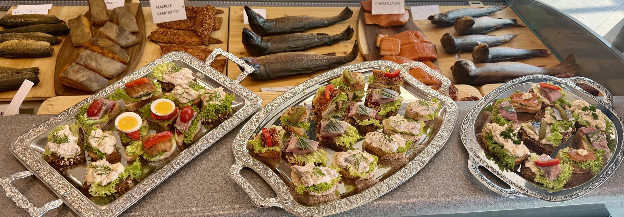 Catering-Auswahl von Morelle — drei silberne Platten mit Fisch-Canapés vor der Räucherfisch-Theke