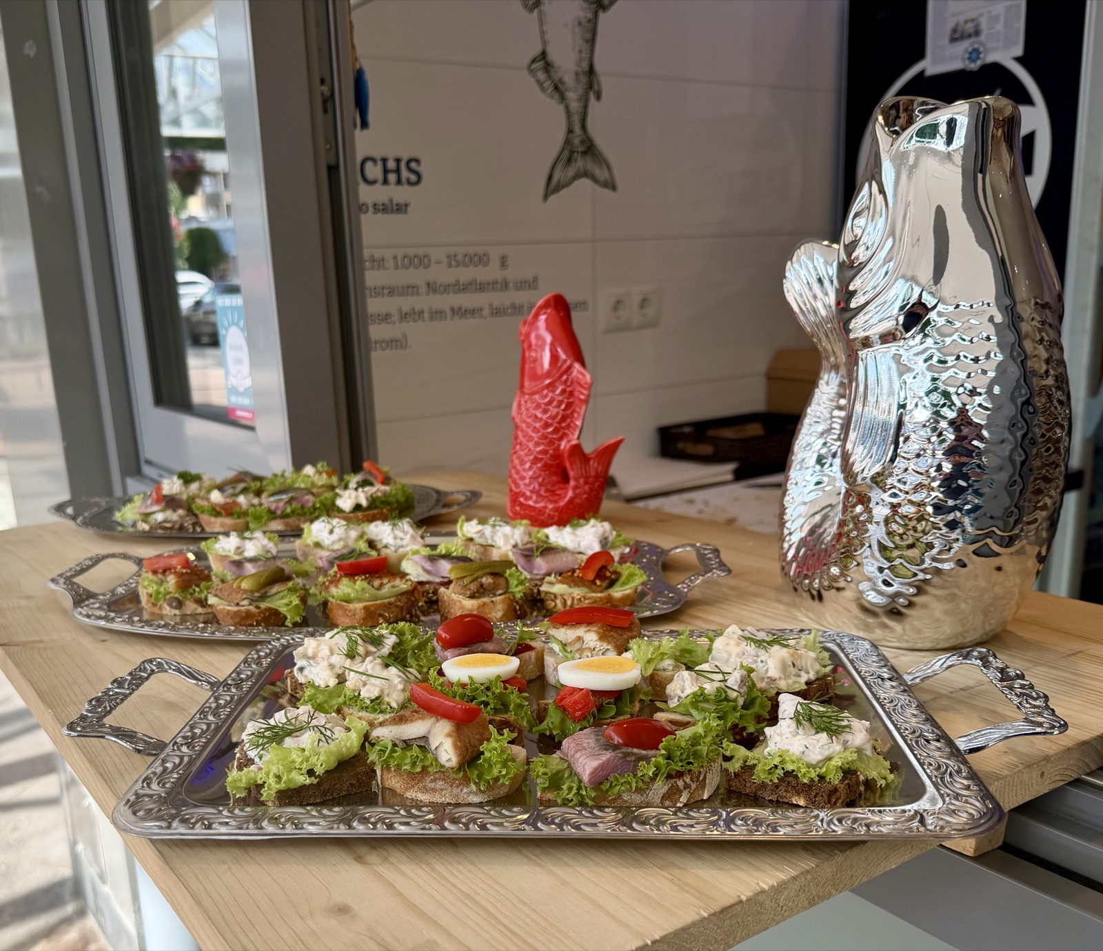 Catering von Morelle — silbernes Tablett mit Fisch-Canapés auf dem Holztresen, im Hintergrund die Morelle-Schaufensterscheibe