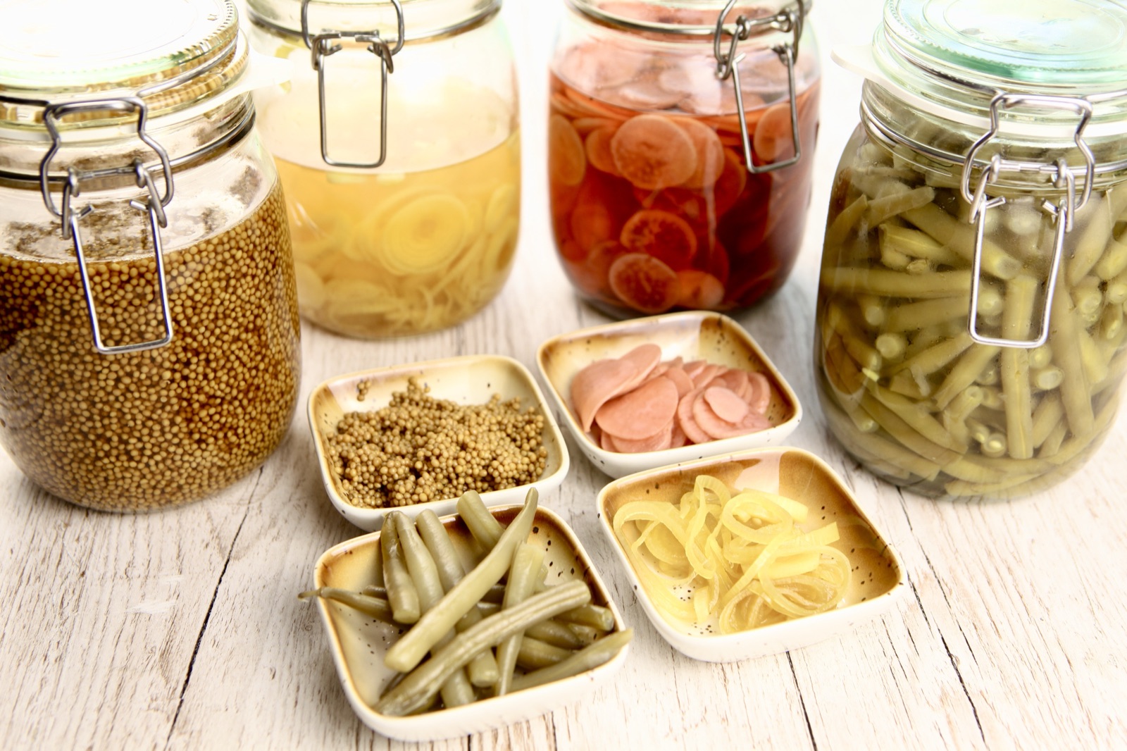 Hausgemachte Toppings von Morelle — Einmachgläser mit Senfkaviar, eingelegten Zwiebeln, Radieschen und grünen Bohnen, dazu kleine Schälchen mit selbst Eingelegtem